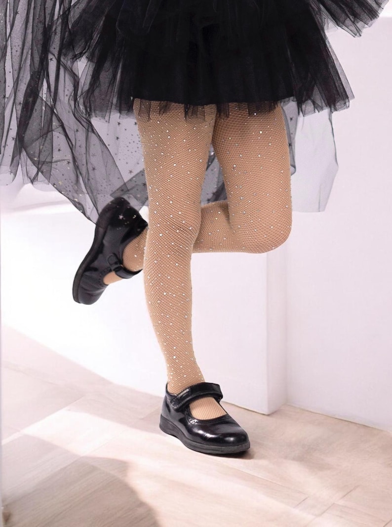K&ouml;nnte beinhalten: Eine nude farbene Netzstrumpfhose mit kleinen wei&szlig;en Strasssteinen. Die Strumpfhose wird von einer Person getragen, die schwarze Schuhe und einen schwarzen T&uuml;llrock tr&auml;gt.