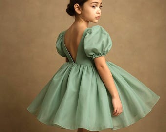 Può includere: Un vestito verde salvia con schiena scoperta e maniche corte a sbuffo. L'abito ha una gonna svasata ed è realizzato in un tessuto leggero. La ragazza indossa l'abito e guarda di lato. Ideale per un'occasione speciale.
