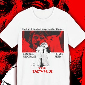 Pode incluir: Camiseta branca com um gráfico preto e vermelho de um pôster de filme para "Os Demônios". O pôster apresenta uma cena do filme com Vanessa Redgrave e Oliver Reed. O texto "Hell will hold no surprises for them..." está no topo do pôster.