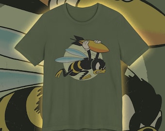 May include: Olive green t-shirt featuring a cartoon bee carrying a bomb. The bee is black and yellow with blue wings, set against a light circle. The design has a vintage, animated style.
