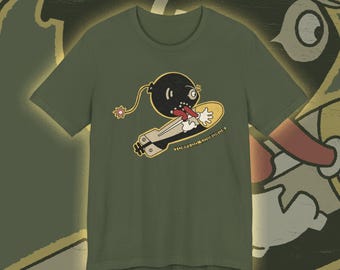 May include: Olive green t-shirt featuring a cartoon bomb character riding a torpedo. The bomb has a surprised expression with its tongue sticking out. The text "TORPEDO SQUADRON" is printed below the torpedo in a vintage style.