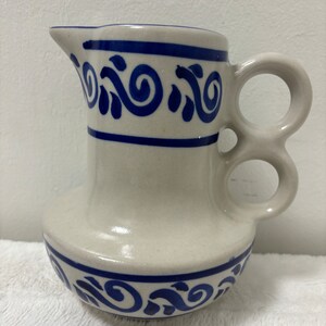 May include: A white ceramic pitcher with a blue and white swirl design. The pitcher has a double handle and a rounded base.