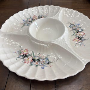 May include: White ceramic serving platter with a scalloped edge and floral accents. The platter is divided into four sections, including a central bowl. The floral design features pink, blue, and green flowers.