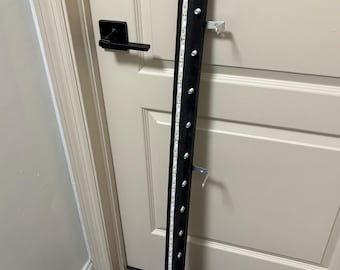 May include: A long, narrow black metal bar featuring a vertical strip of LED lights running down its center. The bar is equipped with a series of small, evenly spaced silver-colored cylindrical studs and includes two metal L-shaped mounting brackets.