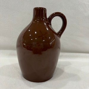 May include: A brown ceramic pitcher with a handle. The pitcher has a rounded body and a small opening at the top.