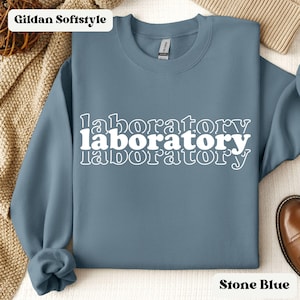 Puede incluir: Sudadera azul piedra con el texto "laboratory" repetido tres veces en una fuente retro blanca.