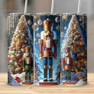 May include: Three stainless steel tumblers with a Christmas theme. Each tumbler features a Nutcracker standing in front of a decorated Christmas tree with ornaments and lights. The background is a dark blue with white snowflakes.