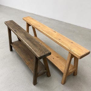 May include: Two wooden benches. One is stained a dark brown, the other is a light natural wood color. Both have a shelf and angled legs. The benches are made of wood and are suitable for indoor or outdoor use.