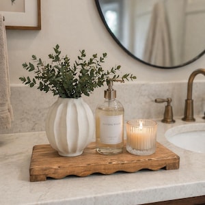 Könnte beinhalten: Ein Holztablett trägt eine weiße Vase mit Grün, einen transparenten Seifenspender mit der Aufschrift "Sandalwood" und eine brennende Kerze in einem Glas. Die Gegenstände stehen auf einer Marmorarbeitsplatte in einem Badezimmer.
