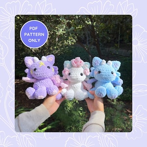 May include: Three crocheted dragon plushies in different colours: purple, white, and blue. Each dragon has a unique design and features a cute, whimsical expression.  PDF PATTERN ONLY.