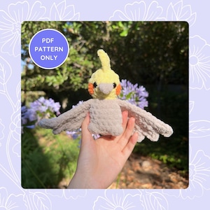 Può includere: Un giocattolo di peluche di cacatua ninfa lavorato a uncinetto con piumaggio giallo e grigio. L'uccello ha accenti arancioni intorno agli occhi e un piccolo becco.