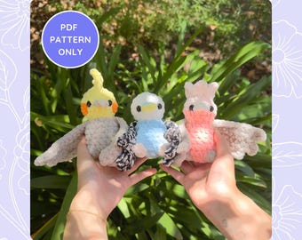 Op de afbeelding: Drie gehaakte amigurumi vogelknuffels. De vogels zijn een gele en grijze kaketoe, een lichtblauwe vogel en een roze en witte kaketoe. De knuffels worden in de handen van een persoon gehouden.