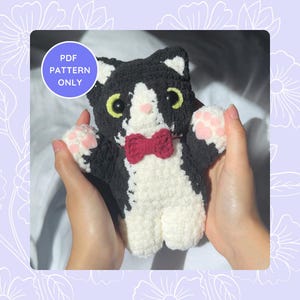 May include: A handmade crochet cat in black and white with a red bow tie. The cat has pink paw pads and green eyes. The text "PDF PATTERN ONLY" is in a blue circle.