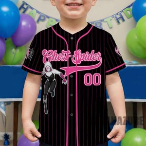 May include: Black baseball jersey with pink pinstripes, featuring the text "Ghost Spider" in pink script, the number "00", and a graphic of a female superhero. The jersey has a button-up front and short sleeves.