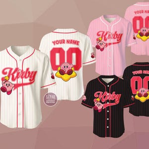 Może przedstawiać: Koszulki baseballowe w kolorze białym, różowym i czarnym, z napisem "Kirby" w stylizowanej czcionce, postacią z kreskówki i możliwością dodania imienia i numeru. Koszulki mają czerwone akcenty i pinstripes.