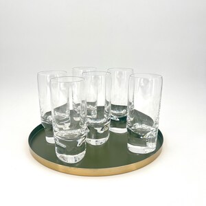 Peut inclure: Six verres à boire transparents avec un fond arrondi sont disposés en cercle sur un plateau vert et or.