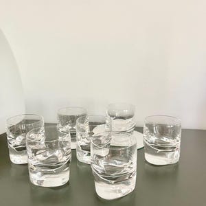 Peut inclure: Ensemble de huit verres à boire courts et transparents. Les verres présentent un design texturé et ondulé. Ils sont disposés sur une surface gris foncé, avec un fond blanc. Idéal pour les boissons.