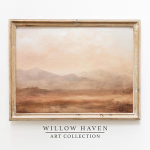 May include: A framed landscape painting with a warm color palette. The artwork depicts a mountain range in shades of brown, beige, and orange, with a hazy sky. The frame is a light, distressed wood. The text "WILLOW HAVEN ART COLLECTION" is at the bottom.