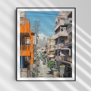 Op de afbeelding: Een smalle straat in een Japanse stad met hoge gebouwen aan beide kanten. De gebouwen zijn een mix van oranje en grijs, en er lopen bovenleidingen overheen. De straat is leeg behalve voor een enkele auto in de verte.