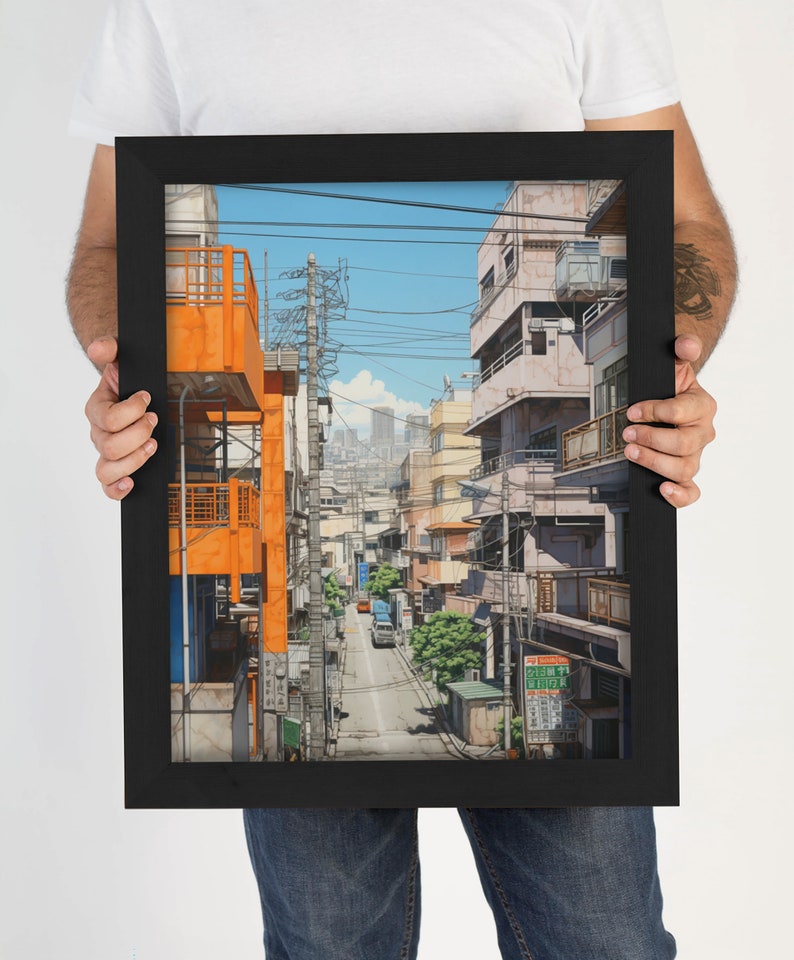 Op de afbeelding: Een ingelijste illustratie van een smalle straat in een Japanse stad. De straat is omzoomd met gebouwen, waarvan sommige oranje geverfd zijn. Er lopen bovengrondse stroomleidingen en een auto rijdt over de straat.