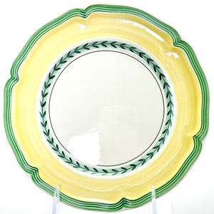 May include: A decorative plate with a scalloped edge. The plate features a yellow and green rim, a white center, and a green leaf design around the inner edge. The plate is designed for serving food.