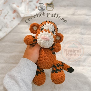 May include: A crochet pattern PDF featuring a plush tiger toy made of orange yarn with black stripes, a white muzzle, and a pink nose. The tiger has rounded ears, small arms, and a long tail. The text "crochet pattern" and "Neutral Knots" are visible.