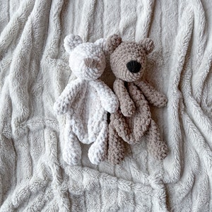 May include: Two crocheted teddy bears on a white fluffy blanket. One bear is white and the other is brown.