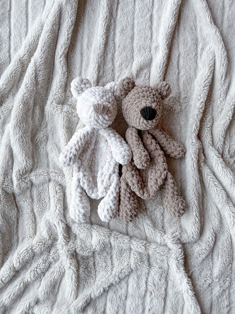 May include: Two crocheted teddy bears on a white fluffy blanket. One bear is white and the other is brown.