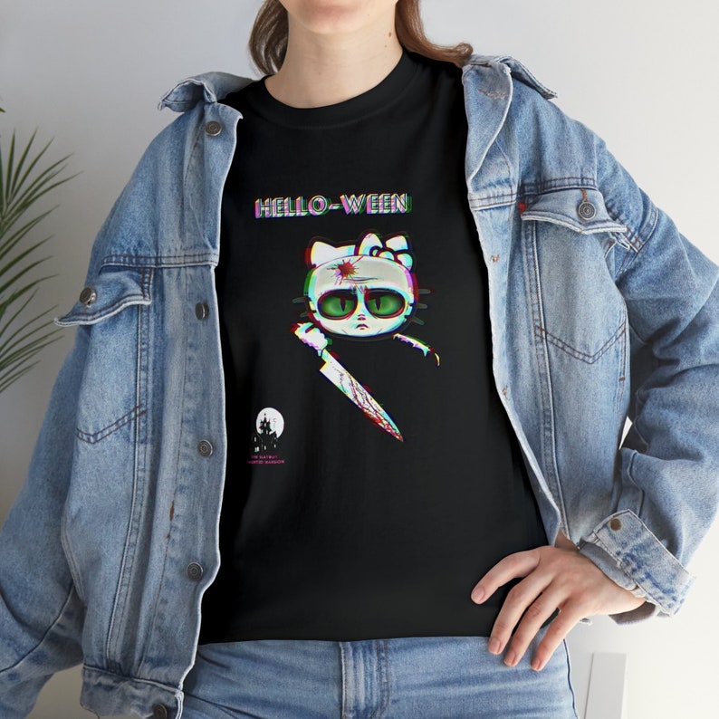 May include: Black t-shirt with a cartoon cat design, green eyes, and a bloody knife. The text "HELLO-WEEN" is above the cat, with a haunted house and moon graphic below. The shirt is worn with a denim jacket.
