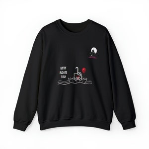 Op de afbeelding: Zwart sweatshirt met een afbeelding van Hello Kitty in een boot met een rode ballon. De tekst "KITTY FLOATS TOO" staat op de voorkant. Een kleine afbeelding van een spookhuis en maan staat rechtsboven.