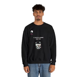 Op de afbeelding: Zwarte sweatshirt met een afbeelding van een kat met een hoed en gestreept shirt, met de tekst "12 Kitty's Coming For You". Een kleine afbeelding van een maan en een kasteel staat boven de tekst.