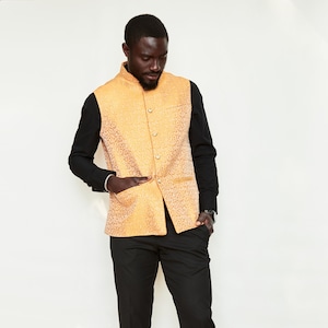 May include: A man wearing a gold patterned vest over a black long-sleeved shirt, black pants, and black shoes.