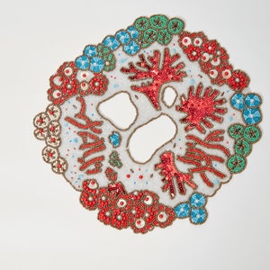 May include: A white fabric circle with red, blue, and green beaded designs. The design features coral, seaweed, and other sea life.
