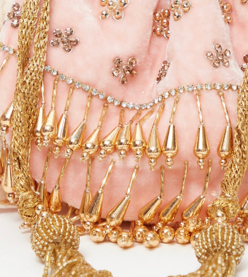 K&ouml;nnte beinhalten: Eine rosa Samt-Kordeltasche mit goldenen und silbernen Verzierungen. Die Tasche hat einen Fransen aus goldenen Perlen und einen goldenen Quasten.