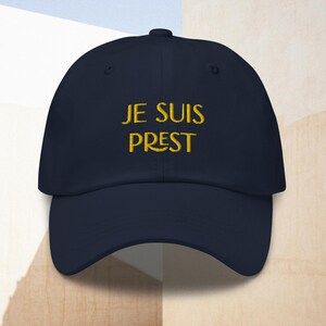 May include: A navy blue baseball cap with the phrase "JE SUIS PREST" embroidered in yellow.