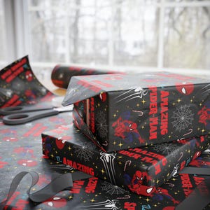 May include: Black wrapping paper featuring Spider-Man graphics, including the character, spiderwebs, and the words "AMAZING SPIDER-MAN" in red. The paper is used to wrap gifts, with scissors and ribbon nearby.