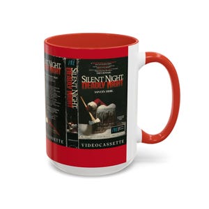 May include: A white ceramic mug with a red interior and handle. The mug features a movie poster design for "Silent Night, Deadly Night." The poster shows a snowy scene with Santa Claus and the text "Santa's Here."