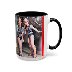May include: White ceramic mug with a black interior and handle. The mug features a retro image of two people in futuristic costumes with helmets and blue bodysuits. A red stripe runs down the side of the mug.