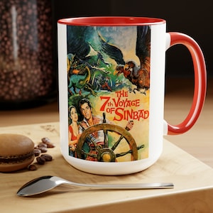 May include: White ceramic coffee mug with a red rim and handle. The mug features a vintage movie poster for "The 7th Voyage of Sinbad" with a colourful illustration of a ship, a giant bird, and a man holding a steering wheel.