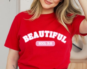May include: Red t-shirt with the word "BEAUTIFUL" in white letters with a pink outline. The text "ECCL 3:11" is in a pink rectangle below the word "BEAUTIFUL".