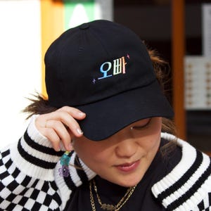 May include: A black baseball cap with a rainbow embroidered design that says "오빠" in Korean.