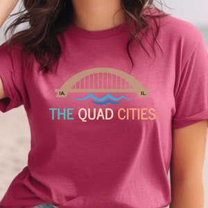 May include: A heather raspberry t-shirt with a graphic of a bridge over water and the text "THE QUAD CITIES".