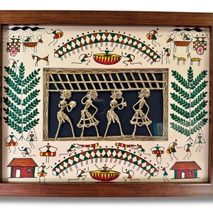 May include: A framed artwork depicting a traditional Indian folk art scene with a central panel of four figures playing instruments. The figures are made of brass wire and are set against a blue background. The surrounding artwork is painted in a whimsical style with figures, animals, and geometric patterns in shades of green, red, brown, and white.