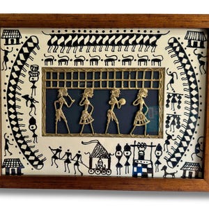 May include: A framed artwork depicting a traditional Indian folk art scene with black and white figures and a gold-coloured metal panel with figures in the centre. The artwork is set against a white background.
