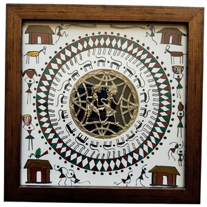 May include: A framed artwork with a white background and a circular design in the center. The design features a gold metal cutout of two figures dancing, surrounded by a black background. The outer circle is decorated with a repeating pattern of green, red, and white triangles, and black lines. The artwork is surrounded by a brown wooden frame.