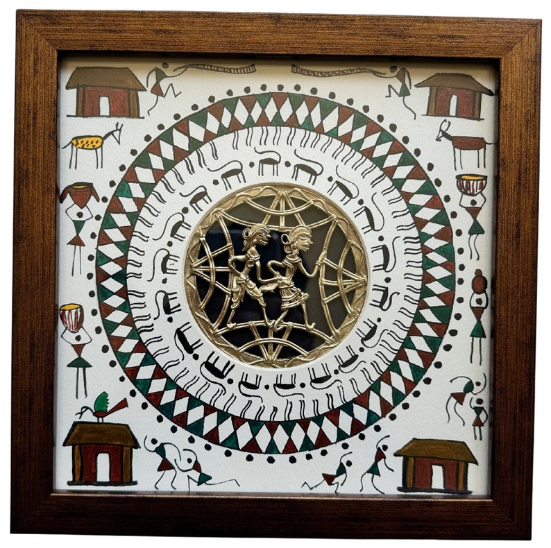 May include: A framed artwork with a white background and a circular design in the center. The design features a gold metal cutout of two figures dancing, surrounded by a black background. The outer circle is decorated with a repeating pattern of green, red, and white triangles, and black lines. The artwork is surrounded by a brown wooden frame.