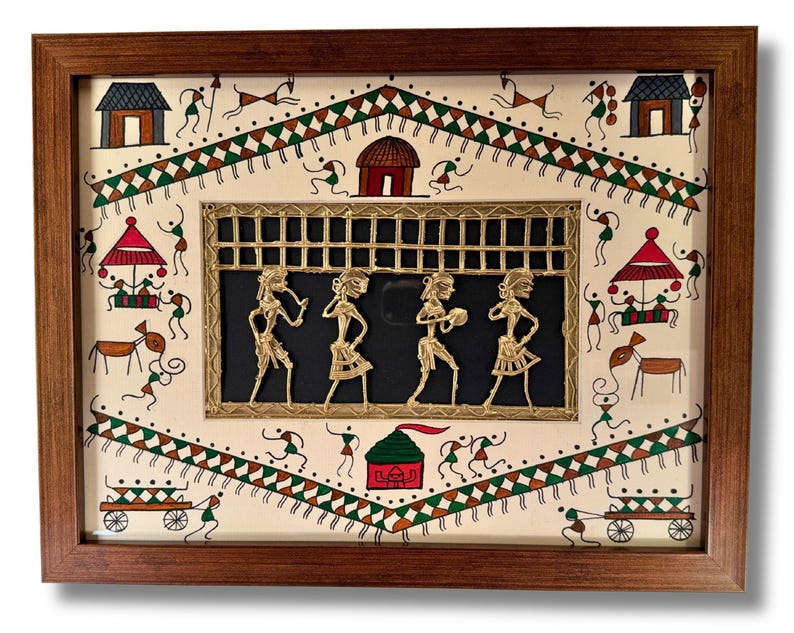 May include: A framed artwork featuring a traditional Indian folk art scene with a central panel of four figures in gold metalwork. The figures are dancing and playing instruments. The background is painted with a white background and colourful geometric patterns.