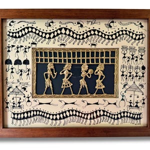 May include: A framed artwork featuring a black and white drawing of people and animals. The artwork is surrounded by a brown wooden frame. A gold metal cutout of four figures is in the centre of the artwork.