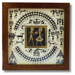 May include: A framed artwork featuring a black and white drawing of a tribal scene with a gold metal cutout of two figures in the center. The artwork is set against a white background and has a brown wooden frame.