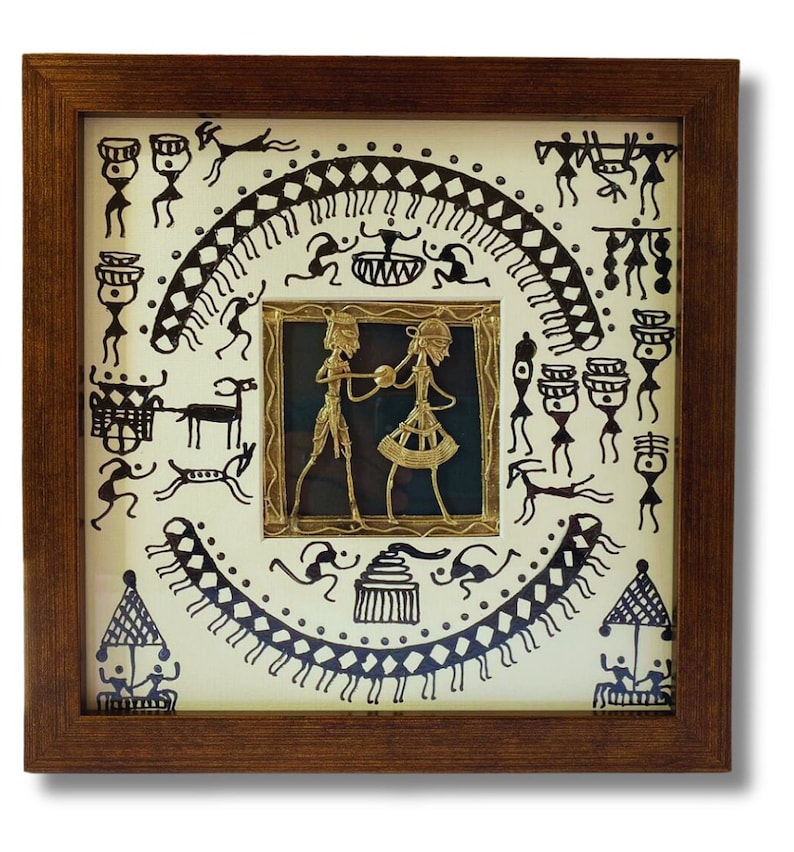 May include: A framed artwork featuring a black and white drawing of a tribal scene with a gold metal cutout of two figures in the center. The artwork is set against a white background and has a brown wooden frame.